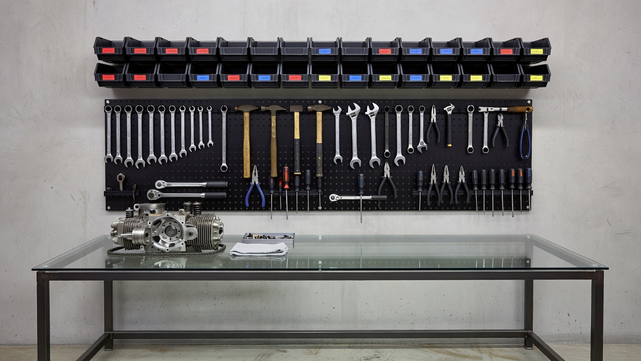 Wall-mounted hand tools and labeled storage above a clear motorcycle workshop bench